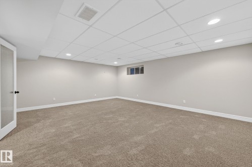Spacious room featuring neutral carpeting, light-toned walls, recessed lighting, and a drop ceiling - 64 South Creek Wynd, Stony Plain, AB 