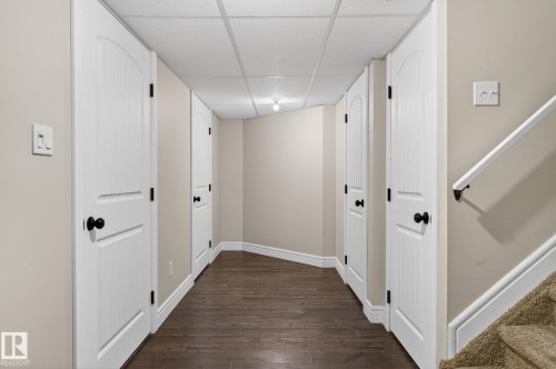 Hallway featuring wood-finish flooring, drop ceiling, white trim, and white doors with matte black hardware - 64 South Creek Wynd, Stony Plain, AB 