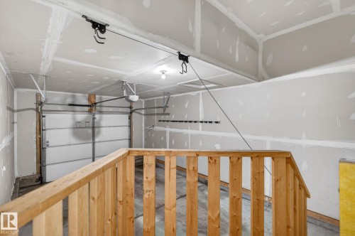 Interior garage space featuring a wooden handrail, overhead garage door, automatic garage door opener, concrete flooring, and unfinished drywall - 64 South Creek Wynd, Stony Plain, AB 