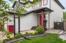 White siding exterior with a contrasting red front door, covered entry porch, dark trim windows, and an adjacent paver stone patio - 64 South Creek Wynd, Stony Plain, AB 