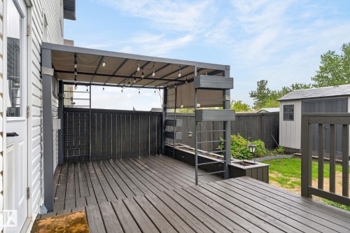 Expansive wood-finish deck with a built-in pergola featuring string lighting - 64 South Creek Wynd, Stony Plain, AB 