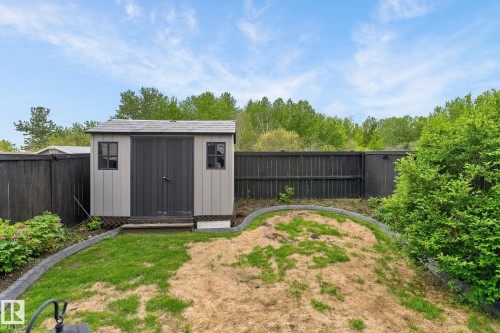 Backyard featuring a shed with grey siding and dark grey trim, a dark wood privacy fence, and concrete curbing defining a garden area - 64 South Creek Wynd, Stony Plain, AB 