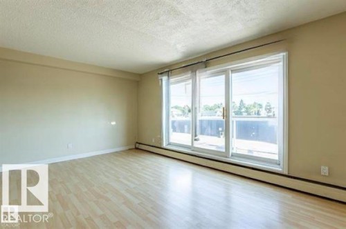 Spacious room featuring light wood-finish flooring, neutral wall tones, and a large sliding glass door - 307 8215 83 Avenue, Edmonton, AB 