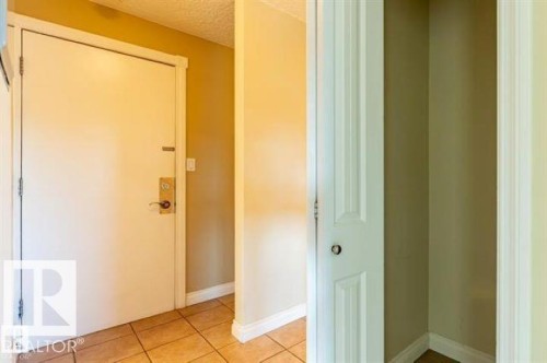 Entryway featuring a white door with brass hardware, ceramic tile flooring, and a recessed storage area with a bi-fold door - 307 8215 83 Avenue, Edmonton, AB 