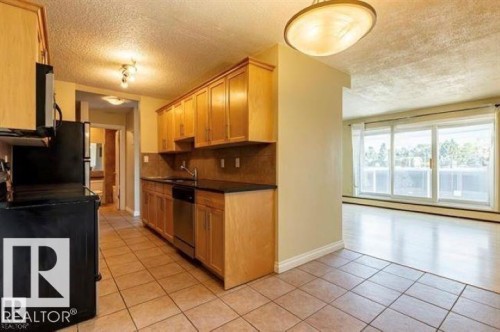 Kitchen featuring wood cabinetry, dark countertops, tiled backsplash, and stainless steel dishwasher - 307 8215 83 Avenue, Edmonton, AB 