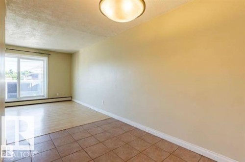Spacious room featuring a sliding glass door, a ceiling-mounted light fixture, light-colored walls, and a combination of wood-finish and tiled flooring - 307 8215 83 Avenue, Edmonton, AB 