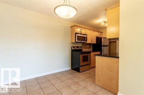 Kitchen area featuring wood-finish cabinetry, stainless steel appliances, and a black countertop - 307 8215 83 Avenue, Edmonton, AB 