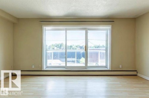 Sliding glass patio door with white trim, light wood-finish flooring, and neutral wall paint - 307 8215 83 Avenue, Edmonton, AB 