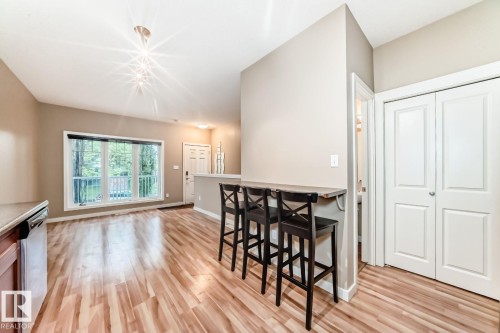 Open-concept living area featuring wood-finish flooring, a contemporary ceiling light fixture, a large window, a built-in breakfast bar, and a bi-fold closet - 4 11917 103 Street, Edmonton, AB 