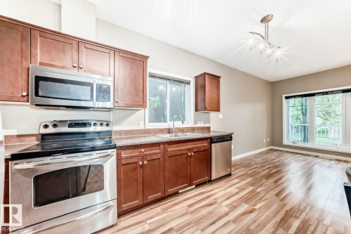 Kitchen featuring wood cabinetry, stainless steel appliances, dark countertops, and wood-finish flooring - 4 11917 103 Street, Edmonton, AB 