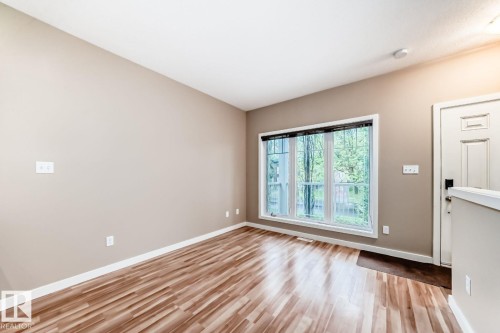 Spacious room with wood-finish flooring, neutral-toned walls, and a large multi-pane window - 4 11917 103 Street, Edmonton, AB 