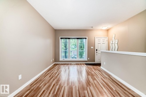 Spacious room featuring wood-finish flooring, a large window with natural light, neutral wall tones, white baseboards, and a paneled entry door - 4 11917 103 Street, Edmonton, AB 