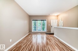 Spacious room featuring wood-finish flooring, a large window with natural light, neutral wall tones, white baseboards, and a paneled entry door - 
