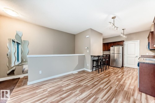 Open-concept living area featuring wood-finish flooring, a contemporary kitchen with stainless steel appliances, dark wood cabinetry, and a breakfast bar - 4 11917 103 Street, Edmonton, AB 