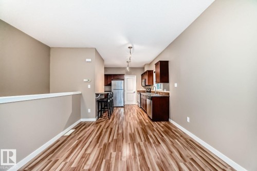 Open-concept living area featuring wood-finish flooring, a neutral color palette, and a functional kitchen with dark cabinetry, stainless steel appliances, and track lighting - 4 11917 103 Street, Edmonton, AB 