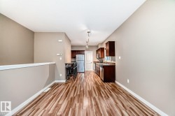 Open-concept living area featuring wood-finish flooring, a neutral color palette, and a functional kitchen with dark cabinetry, stainless steel appliances, and track lighting - 
