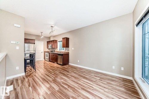 Open-concept living area featuring wood-finish flooring, a kitchen with dark cabinetry, stainless steel appliances, and abundant natural light from a large window - 4 11917 103 Street, Edmonton, AB 