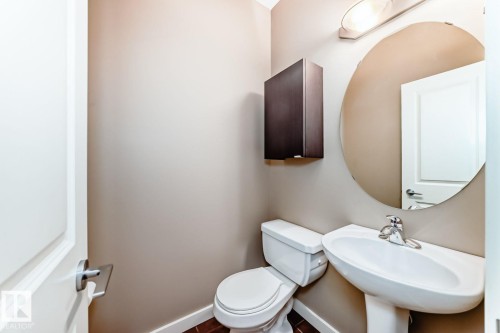 Pedestal sink with chrome faucet, circular wall-mounted mirror, and wall-mounted vanity light fixture - 4 11917 103 Street, Edmonton, AB 