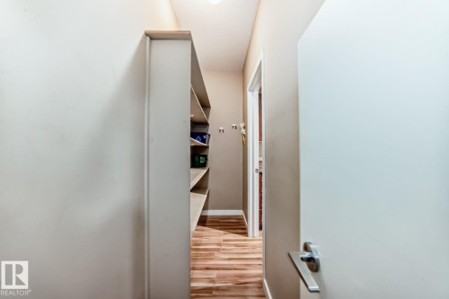 Hallway featuring built-in shelving, wood-finish flooring, recessed lighting, and a white interior door with a brushed nickel lever handle - 4 11917 103 Street, Edmonton, AB 