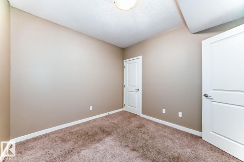 Neutral-toned room featuring two panel doors with satin nickel hardware, plush carpet flooring, painted baseboards, and a ceiling-mounted light fixture - 4 11917 103 Street, Edmonton, AB 