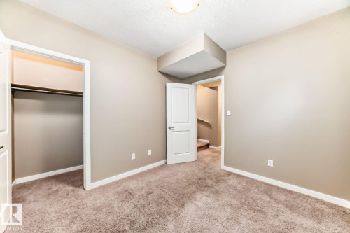 Carpeted room featuring a built-in closet with a hanging rod, neutral wall paint, white trim, and a ceiling-mounted light fixture - 4 11917 103 Street, Edmonton, AB 