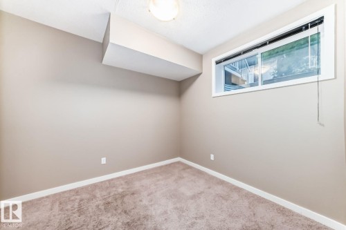 Spacious room featuring neutral paint, white trim, and a window for natural light - 4 11917 103 Street, Edmonton, AB 