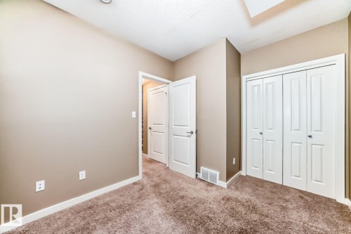 Plush carpeted room featuring a white bi-fold closet, neutral painted walls, white baseboards, and a white paneled door - 4 11917 103 Street, Edmonton, AB 