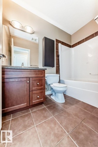 Bathroom featuring a wood-finish vanity with a dark countertop, an integrated sink, and a large wall mirror - 4 11917 103 Street, Edmonton, AB 