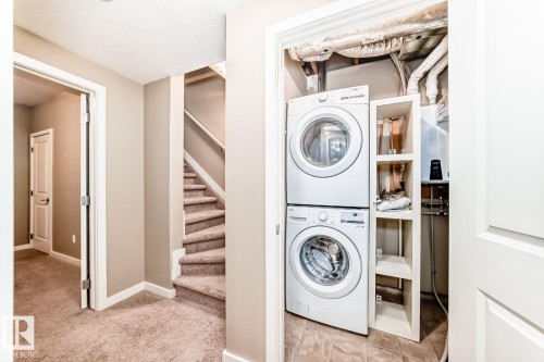 Dedicated utility closet featuring a stacked washer and dryer, integrated shelving, and a wall-mounted water heater - 4 11917 103 Street, Edmonton, AB 
