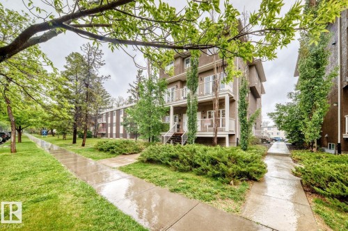 Multi-level building exterior featuring multiple balconies with white railings, a stucco facade, and established landscaping including mature trees and shrubs - 4 11917 103 Street, Edmonton, AB 