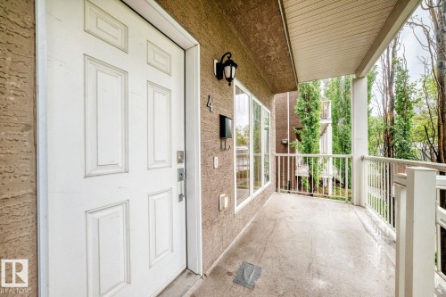Entryway featuring a white paneled door, exterior sconce lighting, multiple windows, a concrete balcony, and white railings - 4 11917 103 Street, Edmonton, AB 