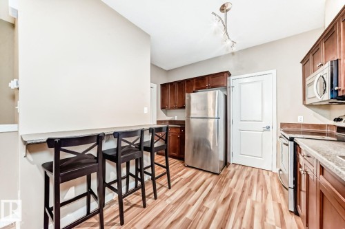 Kitchen featuring wood-finish flooring, stainless steel appliances, dark wood cabinetry, and a breakfast bar - 4 11917 103 Street, Edmonton, AB 