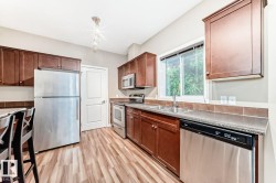 Kitchen featuring wood-finish flooring, stainless steel appliances, dark wood cabinetry, a double basin sink, and a window with natural light - 