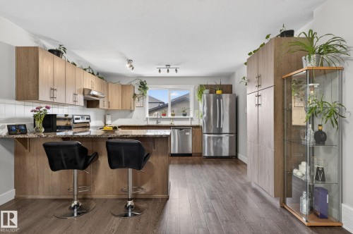 Contemporary kitchen featuring wood-finish cabinetry, stainless steel appliances, a breakfast bar, and wood-finish flooring - 33 Durrand Bend, Fort Saskatchewan, AB 
