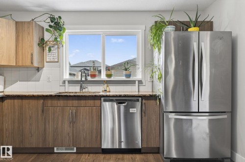 Kitchen featuring wood-finish cabinetry, speckled countertop, white subway tile backsplash, and stainless steel appliances including a built-in dishwasher and a French door refrigerator - 33 Durrand Bend, Fort Saskatchewan, AB 