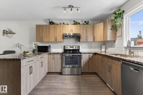 U-shaped kitchen featuring wood-finish cabinetry, stone-finish countertops, stainless steel appliances, and a white subway tile backsplash - 33 Durrand Bend, Fort Saskatchewan, AB 