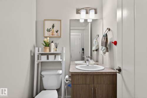 Bathroom featuring an integrated sink with chrome faucet, wood-finish vanity with two-door storage, wall-mounted mirror, and overhead double sconce lighting - 33 Durrand Bend, Fort Saskatchewan, AB 