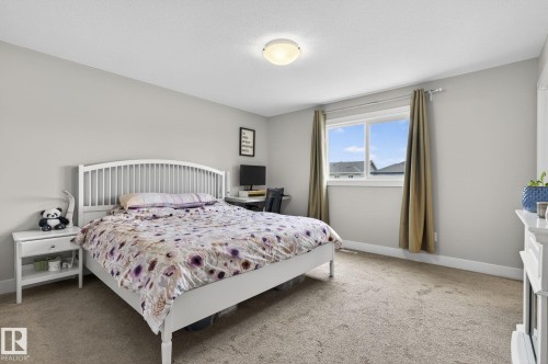 Spacious bedroom featuring light neutral walls, carpet flooring, a large window with white trim, and a flush-mount ceiling light fixture - 33 Durrand Bend, Fort Saskatchewan, AB 