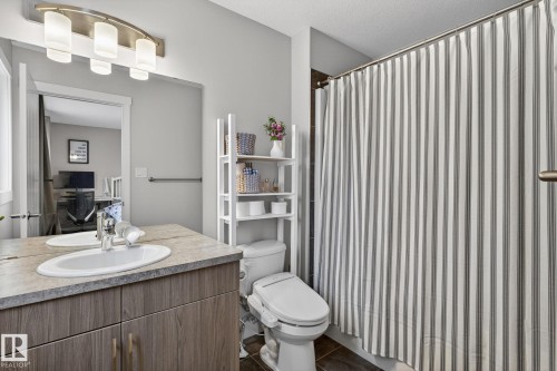 Bathroom featuring a wood-finish vanity with an integrated sink, a neutral countertop, and a contemporary light fixture - 33 Durrand Bend, Fort Saskatchewan, AB 