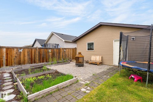 Expansive backyard featuring a natural wood privacy fence, multiple raised garden beds, a gravel patio area, and a stone paver pathway - 33 Durrand Bend, Fort Saskatchewan, AB 