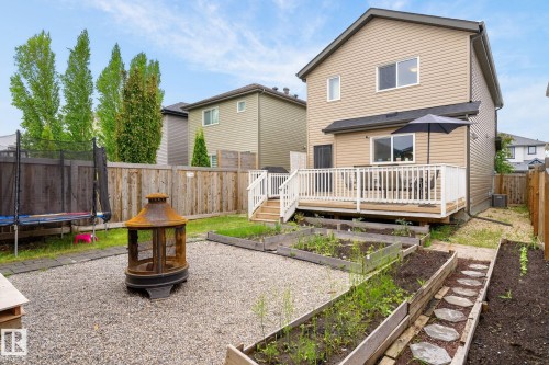 Rear exterior featuring a spacious wood deck with white railings, tan vinyl siding, and a dark shingle roof - 33 Durrand Bend, Fort Saskatchewan, AB 