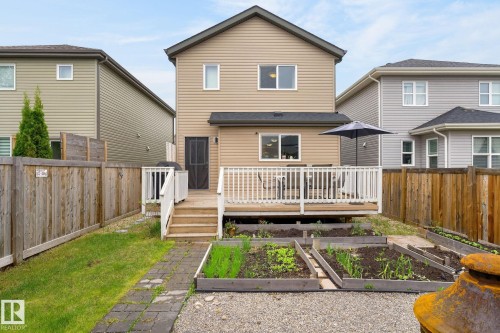 Rear exterior featuring a spacious wooden deck with white railings, steps to the yard, and a screened door access - 33 Durrand Bend, Fort Saskatchewan, AB 