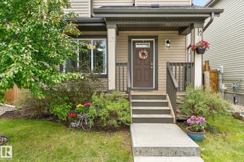 Front entry featuring a covered porch, durable siding, a dark wood-finish door with upper lites, and a concrete pathway - 33 Durrand Bend, Fort Saskatchewan, AB 