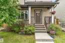 Front entry featuring a covered porch, durable siding, a dark wood-finish door with upper lites, and a concrete pathway - 33 Durrand Bend, Fort Saskatchewan, AB 