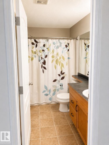 Bathroom featuring a wood-finish vanity with dark countertop, white porcelain sink, and ceramic tile flooring - 115 5340 199 Street, Edmonton, AB - Indoor Photo Showing Bathroom