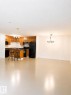 Open-concept kitchen and living area featuring a breakfast bar with seating, black appliances, warm wood cabinetry, and a black chandelier - 115 5340 199 Street, Edmonton, AB  - Indoor Photo Showing Other Room 
