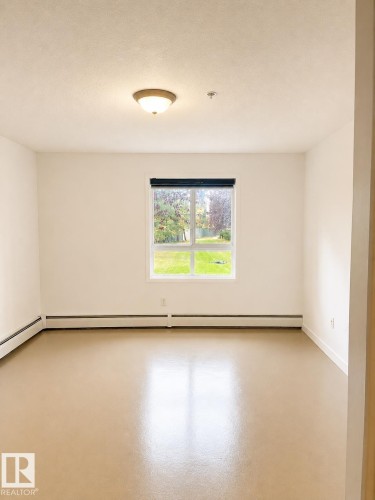 Bright interior space featuring a window with exterior views, light-toned flooring, white walls, and a ceiling-mounted light fixture - 115 5340 199 Street, Edmonton, AB - Indoor Photo Showing Other Room