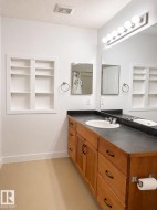 Bathroom featuring a wood-finish vanity with an integrated sink, dark countertop, and large mirror with globe lighting - 