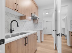 Modern kitchen featuring light wood-finish cabinetry, white countertops, and a stainless steel double-basin sink with a matte black faucet - 