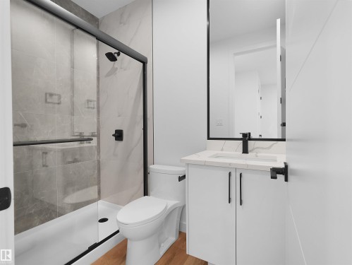 Contemporary bathroom featuring a white vanity with a marbled countertop, black framed mirror, and matte black fixtures - 214 Crystal Creek Drive, Leduc, AB 